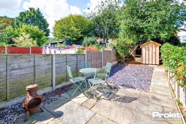 Rear garden laid to grey slate, with patio area, bistro furniture set, and shed