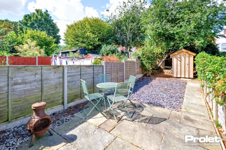 Rear garden laid to grey slate, with patio area, bistro furniture set, and shed