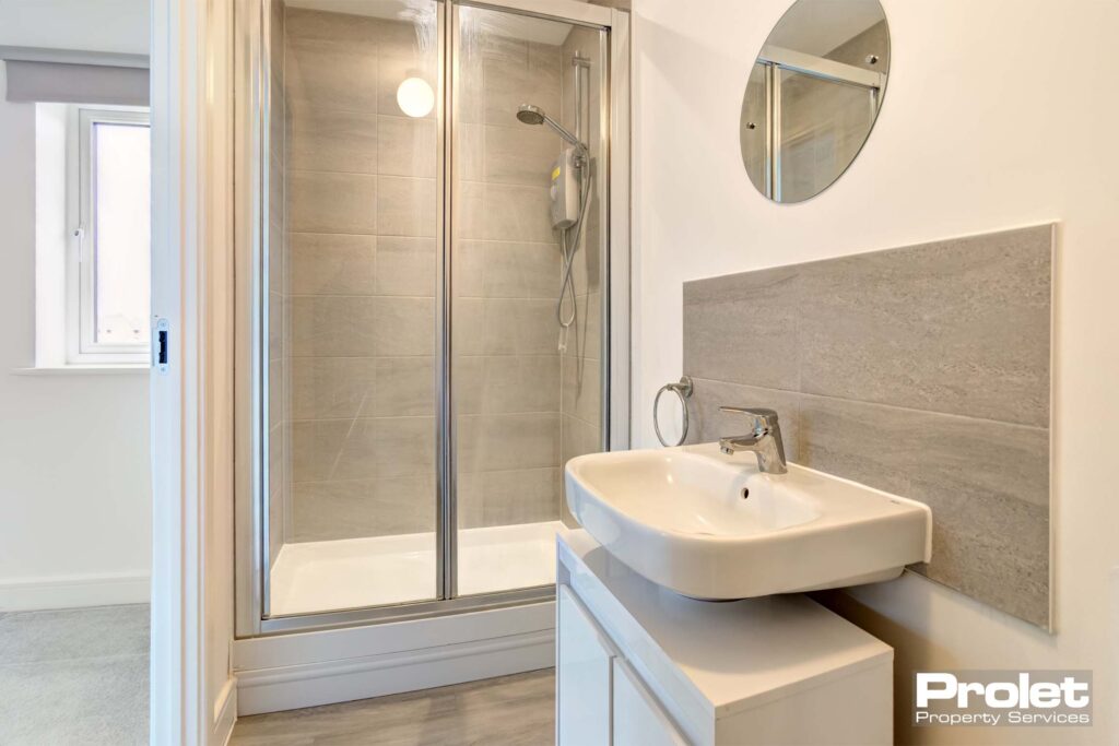 Ensuite bathroom with laminate flooring, shower cubicle with white walls and grey splash back