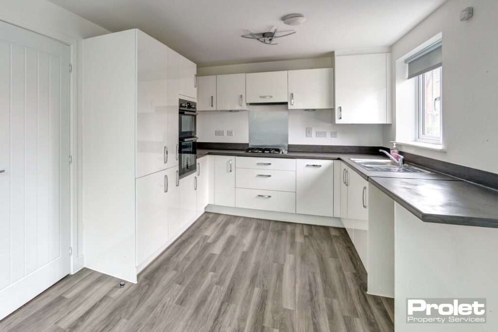 Grey laminate floor to kitchen with white units and grey work top. Integrated double oven and fridge freezer