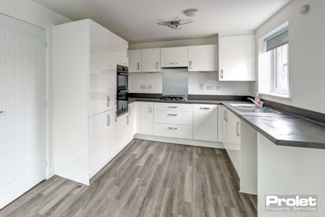 Grey laminate floor to kitchen with white units and grey work top. Integrated double oven and fridge freezer