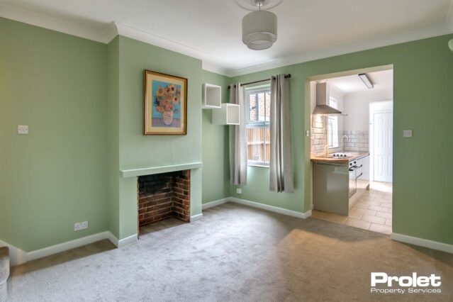 Dining room, leading to kitchen with light grey carpet, green walls, and fireplace
