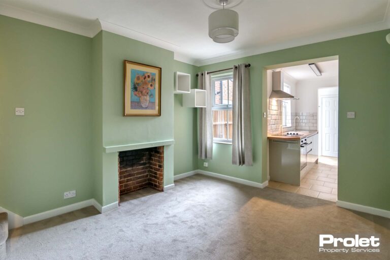 Dining room, leading to kitchen with light grey carpet, green walls, and fireplace