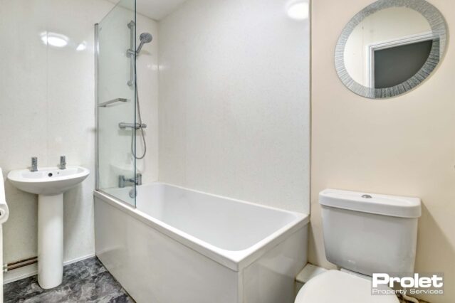 White bathroom suite with shower over bath and mirror over sink