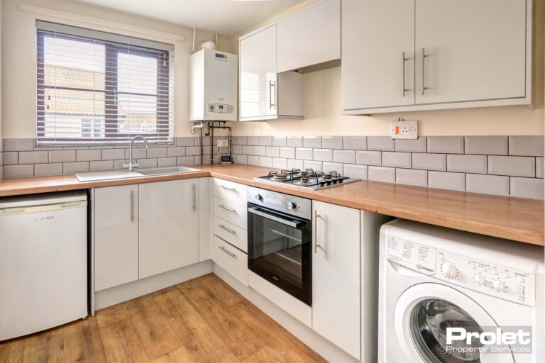 Kitchen with grey walls and magnolia walls. Beech effect work top and flooring with white units. gas hob, electric oveb, single fridge and washing machine