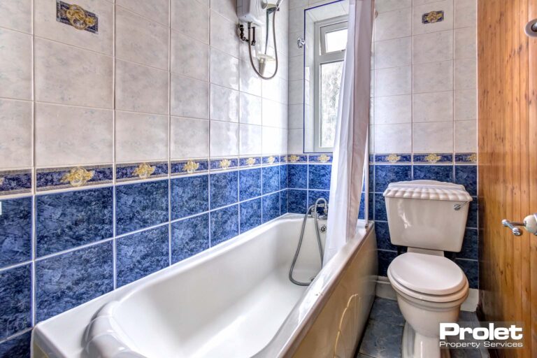 Bathroom with white suite and shower over bath with blue and white wall tiles