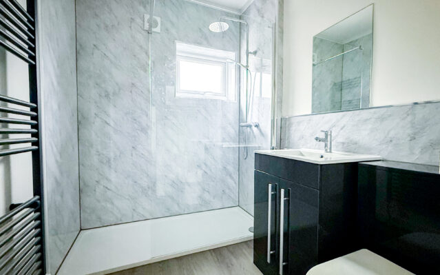 Bathroom with walk in shower, sink with black cabinet, and toilet