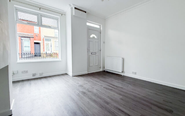 Living room with laminate wood effect flooring, white walls, and UPCV front door.
