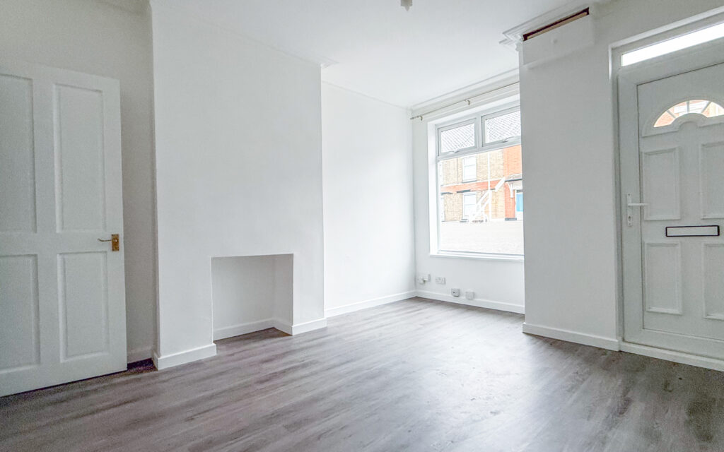 Living room with laminate wood effect flooring, white walls, and UPCV front door.