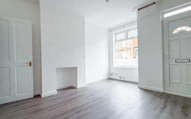 Living room with laminate wood effect flooring, white walls, and UPCV front door.