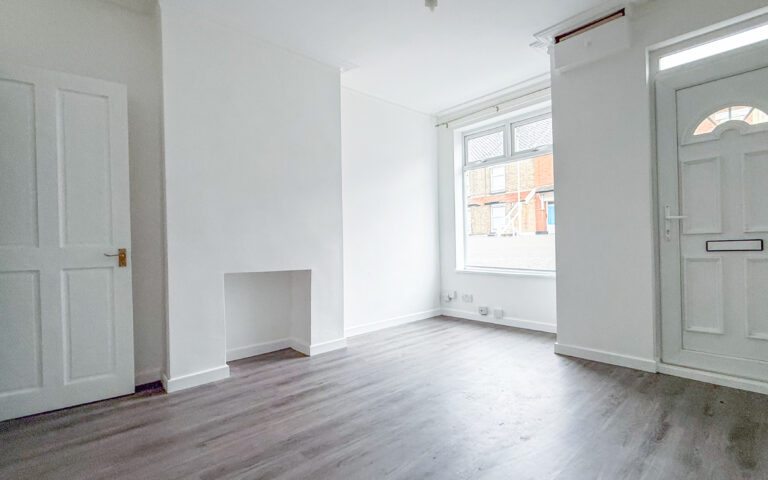 Living room with laminate wood effect flooring, white walls, and UPCV front door.