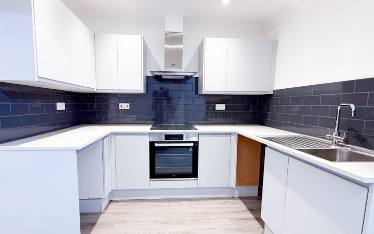 Modern kitchen with white units, white worktops, and black tile backsplash