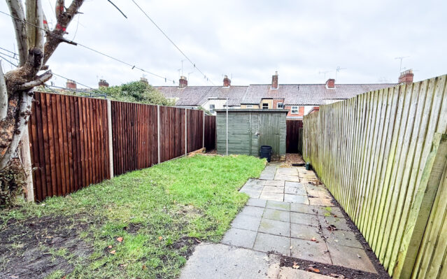 rwar garden with shed, paved path, and lawn.