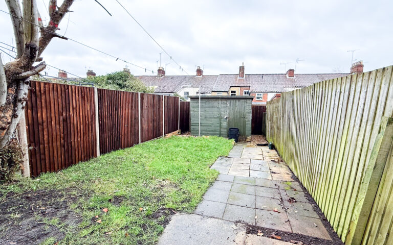 rwar garden with shed, paved path, and lawn.