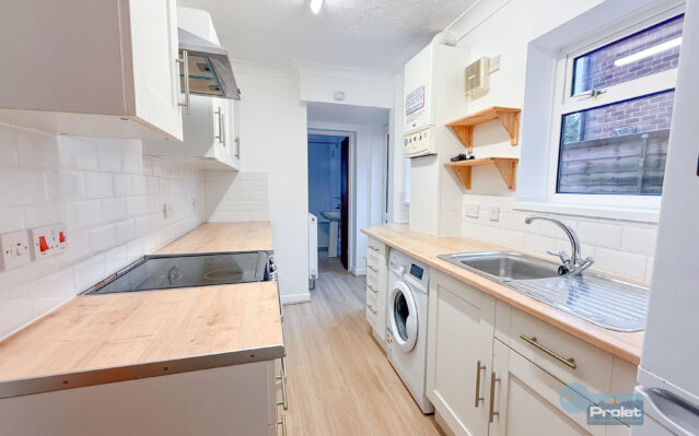 Modern galley kitchen with white cubpoards and wood worktops. Black cooker, and washing machine included.