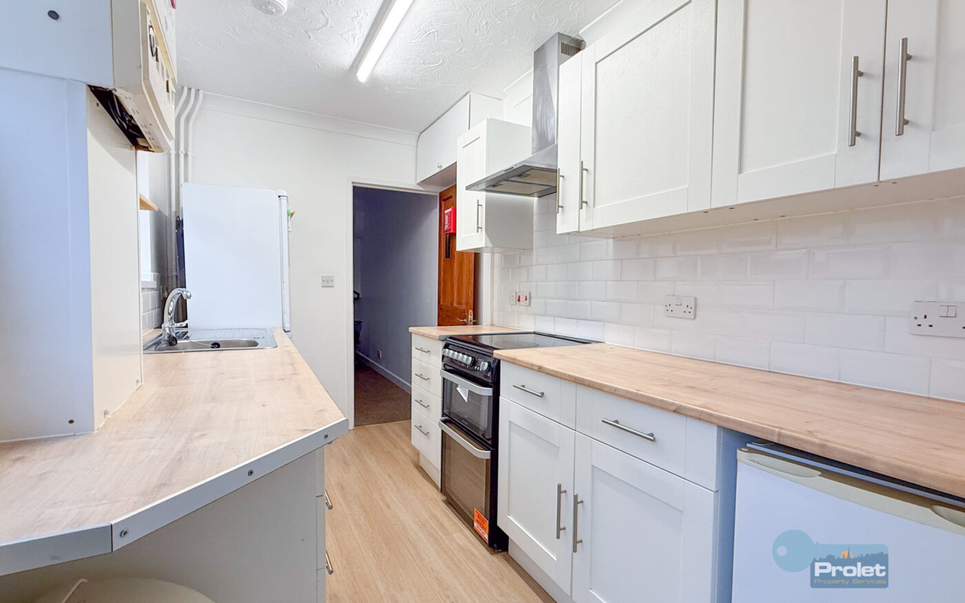 Modern galley kitchen with white cubpoards and wood worktops. Black cooker, and washing machine included.