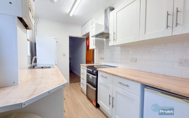 Modern galley kitchen with white cubpoards and wood worktops. Black cooker, and washing machine included.