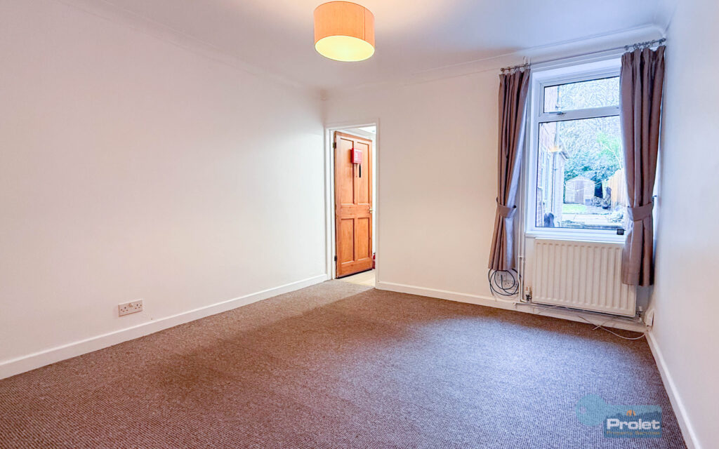 Large lounge with white walls, and brown carpet, leading to kitchen