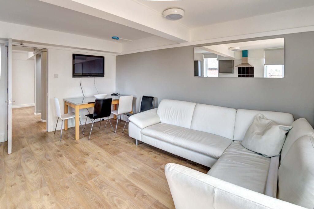 Living area with wall mounted TV, dining table, and white sofas.