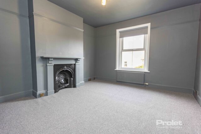 Grey walls and carpet wit feature fireplace large window with venetian blinds