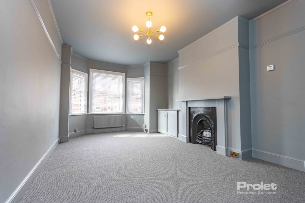Grey walls and carpet wit feature fireplace large window with venetian blinds