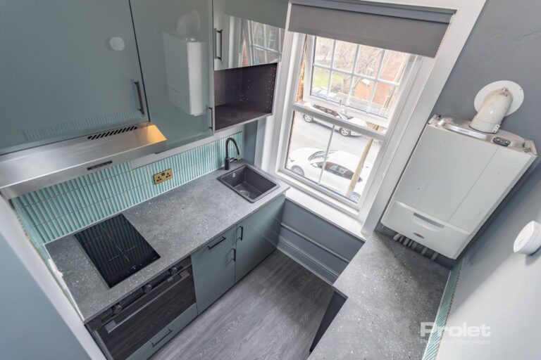 Grey worktops with teal units. Boiler in corner with 2 ring electric hob, oven and undercounter fridge freezer