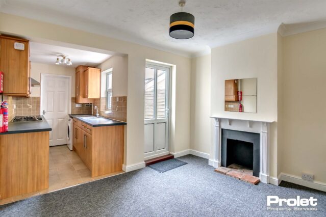 Dining room with grey carpet and magnolia walls opened into fitted kitchen